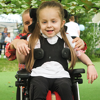 Young student in a wheelchair outside on grass smiling